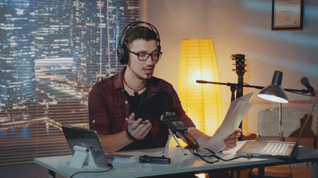 Home recording studio: the speaker in headphone reads the story into the microphone. There is a computer and other recording equipment on the table.の写真素材