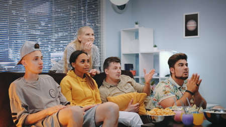 Happy viewers watching sports on TV and spilling popcorn when team scores. They are extremely happy, screaming, jumping and raising clenched fists.の写真素材