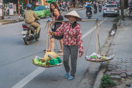 A woman in traditional Vietnamese clothes sells fruits and vegetables in the cityのeditorial素材