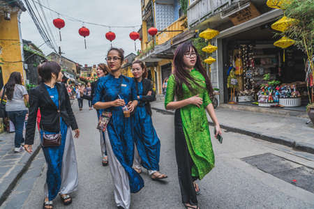 Wonderful view of old street decorated with colorful silk lanterns. Vietnamese people in traditional closes walking along Hoi An Ancient Town. Hoi An (Hoi an), Vietnam - March 12, 2020.のeditorial素材