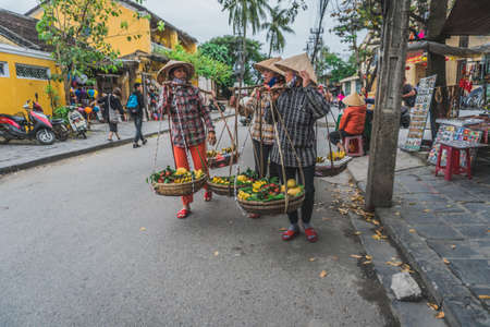Wonderful view of old street decorated with colorful silk lanterns. Vietnamese people in traditional closes walking along Hoi An Ancient Town. Hoi An (Hoi an), Vietnam - March 12, 2020.のeditorial素材