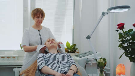 Beautician preparing woman for making facial cleansing in beauty salon. Woman resting after hard...