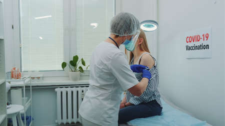 Female doctor in medical protective cloths injecting in womans arm a vaccine against coronavirus. Covid-19 vaccination concept.の写真素材