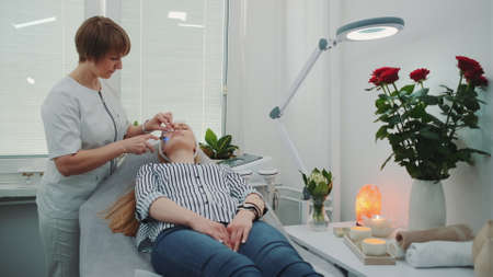 Professional cosmetologist making cavitation peeling on young womans face at beauty salon with modern equipment and pleasant atmosphere.の写真素材