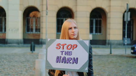 Blonde woman protesting to stop harm by holding steamer and walking on the street. She is upset by what is happening in the world.の写真素材