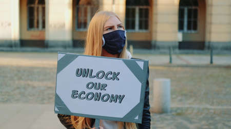 Young woman wearing medical mask calling to unlock the economy by holding steamer. Protest walk in the city center.の写真素材