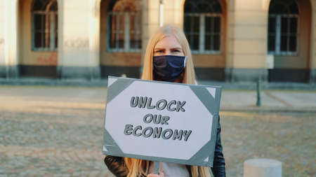 Young woman wearing medical mask calling to unlock the economy by holding steamer. Protest walk in the city center.の写真素材