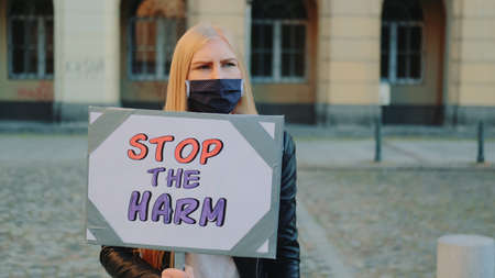 Blonde woman in protective mask protesting to stop harm by holding steamer and walking on the street. She is upset by what is happening in the world.の写真素材