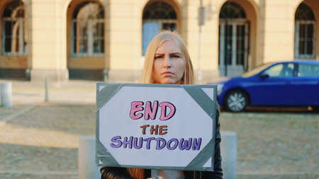 Concerned woman with protest banner calling to end shutdown by walking on the city streetの写真素材
