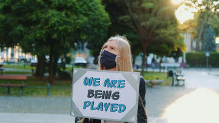 Pretty girl wearing medical mask protesting against authorities that playing human lives. She walking alone in the downtown.の写真素材