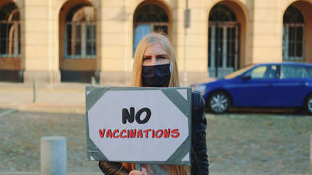 Young woman protesting against vaccination. She worn protective mask and walking down the street