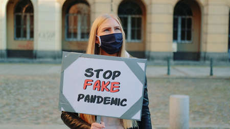 Young woman protesting against fake pandemic. She worn protective mask and walking down the streetの写真素材