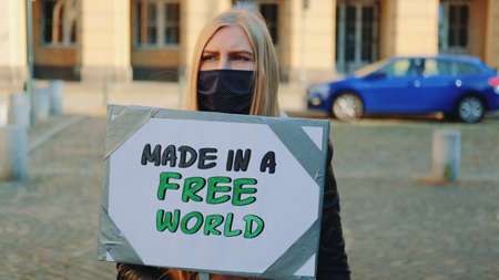 Made in a free world - slogan on protest actions in the city. Young blonde woman in protective mask walking with steamer.の写真素材