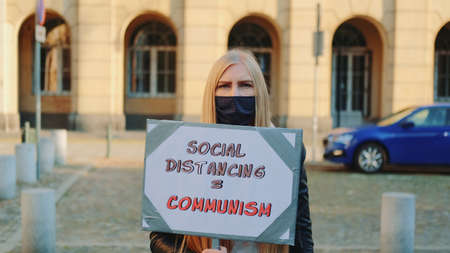 Woman in protective mask protest walk with steamer against social distancing that equals communism. Close-up shot.の写真素材
