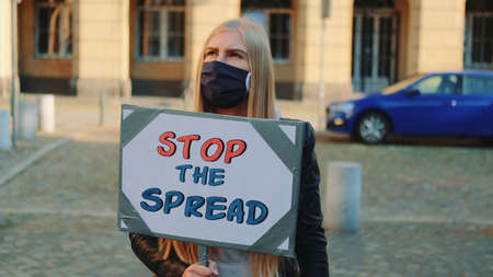 Blonde woman in protective mask calling to stop the spread by holding steamer. Protest walk in the city center.の写真素材