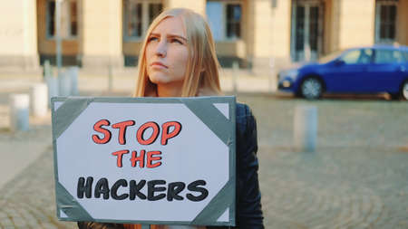 Concerned woman with protest banner calling to stop hackers by walking on the city streetの写真素材