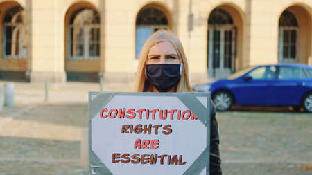 Protest walk: woman in protective mask advocating for constitutional rights protection. She holding banner and going on the street.の写真素材