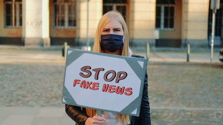 Young woman in protective mask protesting against fake news. She walking down the street with placard.の写真素材