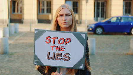 Concerned woman with protest banner calling to stop lies by walking on the city streetの写真素材