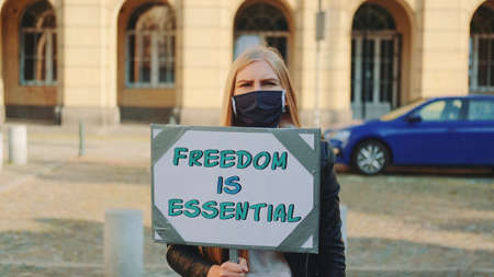 Woman in protective mask on protest walk calling that freedom is essential by walking on the street with banner.の写真素材