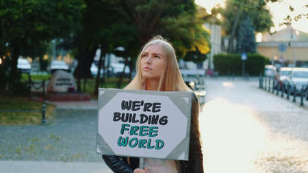Blonde woman holding streamer with slogan BUILDING FREE WORLD on protest walk in the city centerの写真素材