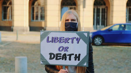 Blonde woman in protective mask with protest banner calling to choose liberty or death. She walking on the street.の写真素材
