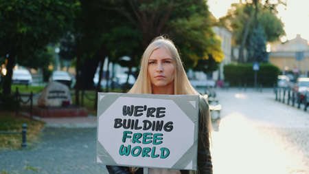 Blonde woman holding streamer with slogan BUILDING FREE WORLD on protest walk in the city centerの写真素材