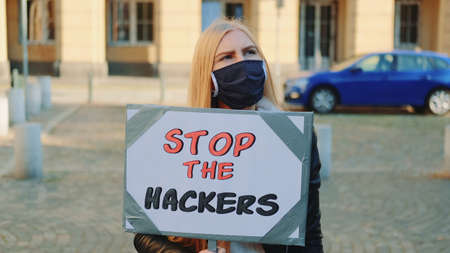 Concerned woman in protective mask with protest banner calling to stop hackers by walking on the city streetの写真素材
