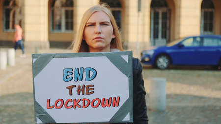 Young woman asking to end lockdown on protest march by walking on the street with banner.の写真素材