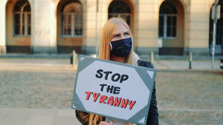 Young woman in protective mask calling to stop the tyranny by holding steamer. Protest walk in the city center.の写真素材