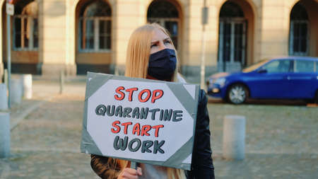 Young woman in protective mask calling to stop quarantine and start working. She worn protective mask and walking down the street.の写真素材