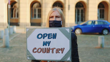Young woman in protective mask calling to open the country on protest walk. She holding steamer and walking on the street.の写真素材