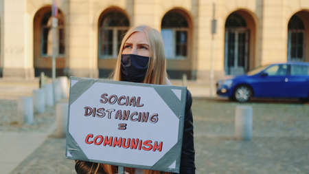 Woman in protective mask protest walk with steamer against social distancing that equals communism. Close-up shot.の写真素材