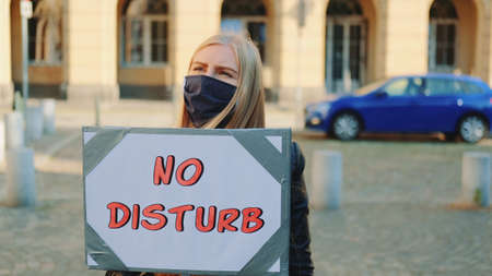 No disturb slogan on protest walk. Woman in protective mask with steamer walking on the street.の写真素材