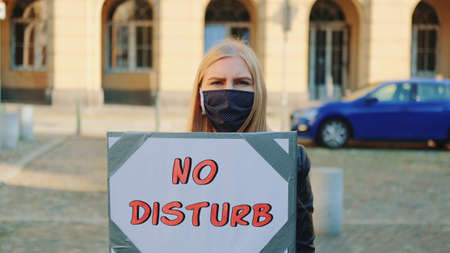 No disturb slogan on protest walk. Woman in protective mask with steamer walking on the street.の写真素材
