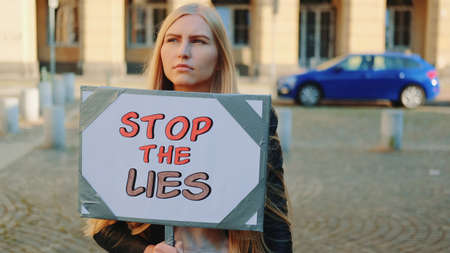 Concerned woman with protest banner calling to stop lies by walking on the city streetの写真素材