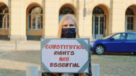 Protest walk: woman in protective mask advocating for constitutional rights protection. She holding banner and going on the street.の写真素材