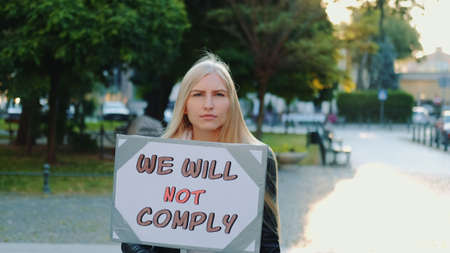 Protest walk: woman holding placard with words that people wont comply. Blonde woman walking alone in city center.の写真素材