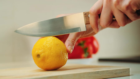 Close-up shot of hands with knife cutting lemon on the kitchen board.の写真素材
