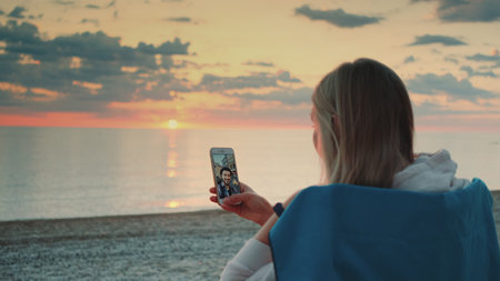 Young woman making video call to her friend with smartphone on the beach. Relaxing and speaking with friends.の写真素材