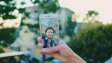 Close-up of man speaking on video call on smartphone. In the background - green trees.の写真素材