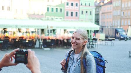 Medium shot of man making photos of female tourist on the view of city market square. Blonde woman making faces and smiling.の写真素材