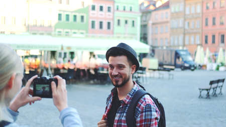 Medium shot of couple of tourists making photos with photo camera on historical market square. Man posing and woman taking photos.の写真素材
