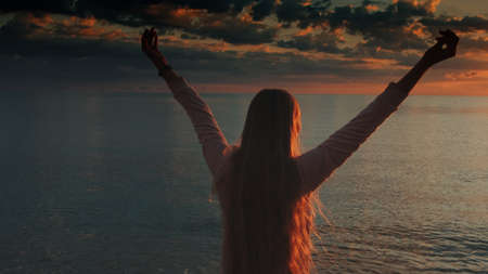 Woman with outstretched arms enjoying the beauty of sunset on the sea. Crane shot.の写真素材