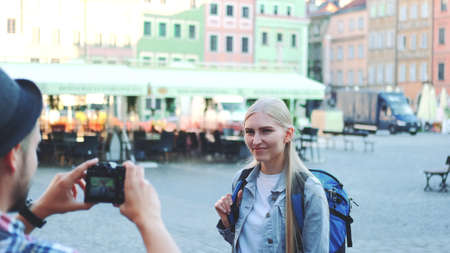 Medium shot of man making photos of female tourist on the view of city market square. Blonde woman making faces and smiling.の写真素材