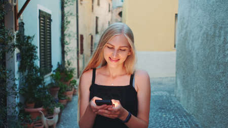 Beautiful young lady chatting on smartphone while walking on the street. Summer evening, empty streets.の写真素材