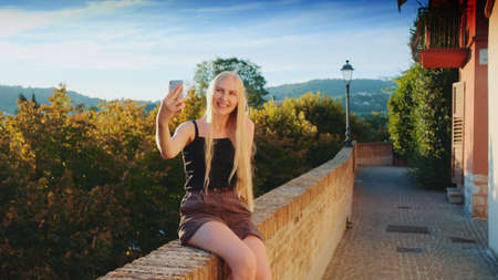 Pretty girl making selfie on smartphone in front of beautiful nature landscape. Summer trip to another country.の写真素材