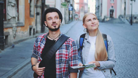 Happy young tourist couple with map walking and looking at old city architecture. Sightseeing in beautiful european city.の写真素材