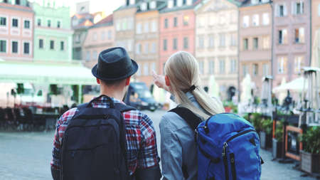 Back view of young tourists couple with bags checking map on central city square. They discussing their new destination.の写真素材