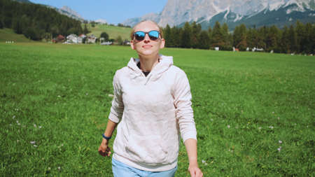 Blonde woman having fun by running in nature field in summer. Mountains in the background.の写真素材